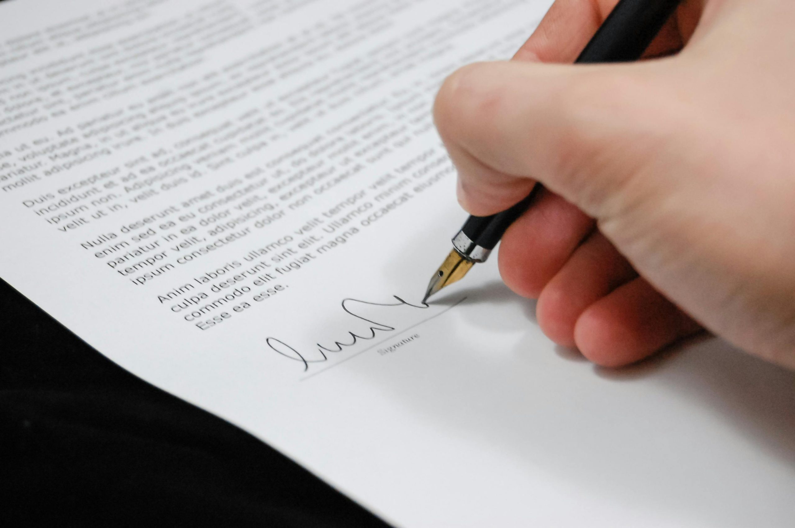 pexels-pixabay-48148 A hand signing a document with a fountain pen in Tampa; the paper contains dense text and a signature line at the bottom.